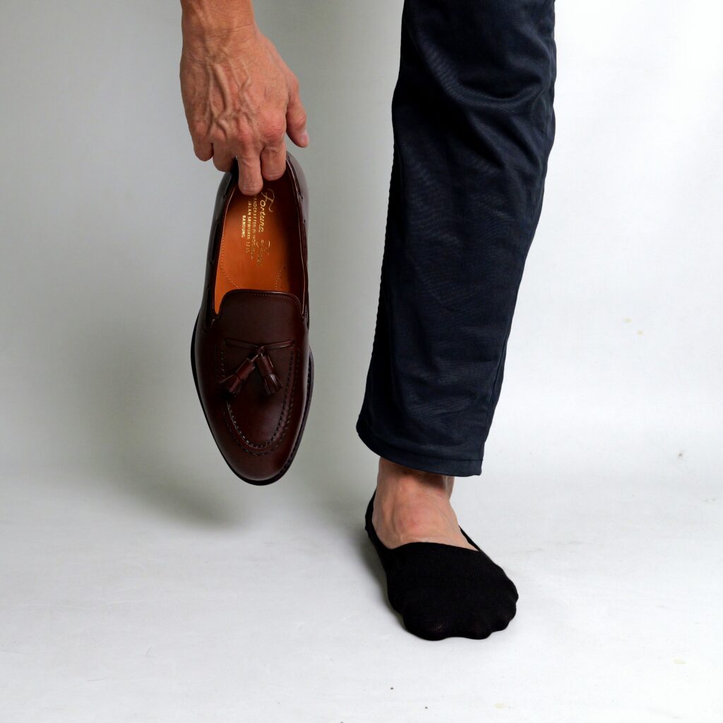 AGAM socks ECLIPSE LoaferFit on left foot with right hand holding shoe